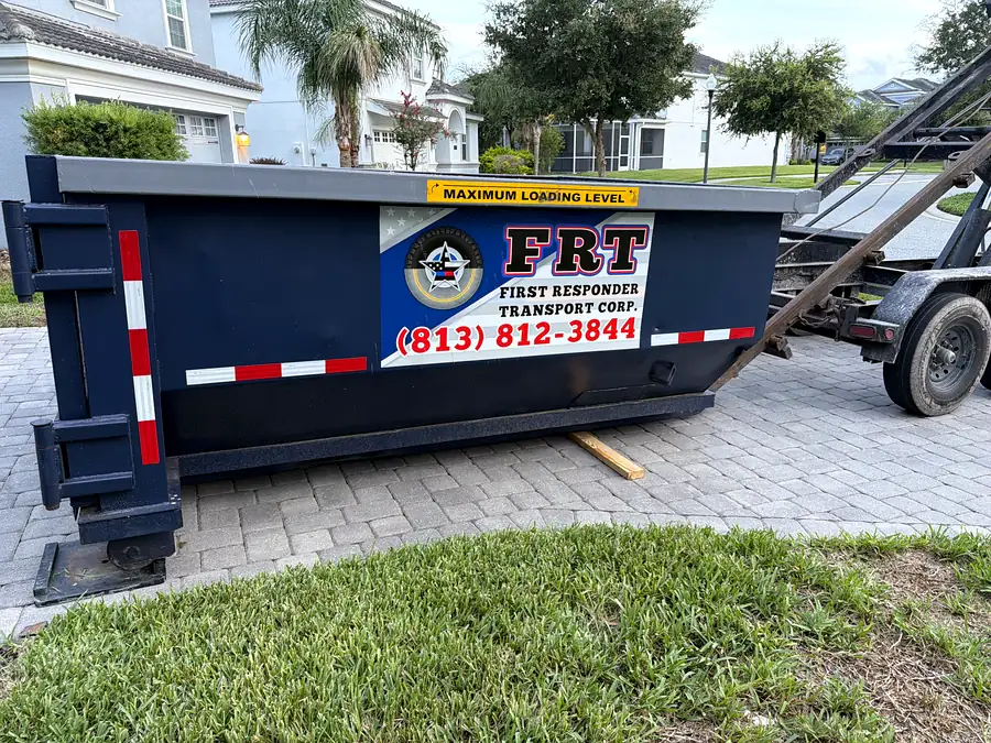 A roll-off dumpster placed on a paver driveway in front of a house